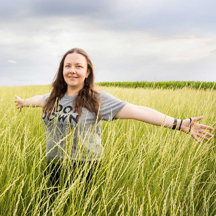 Tessa Peters stands with arms outstretched in the middle of a field of Kernza wheat