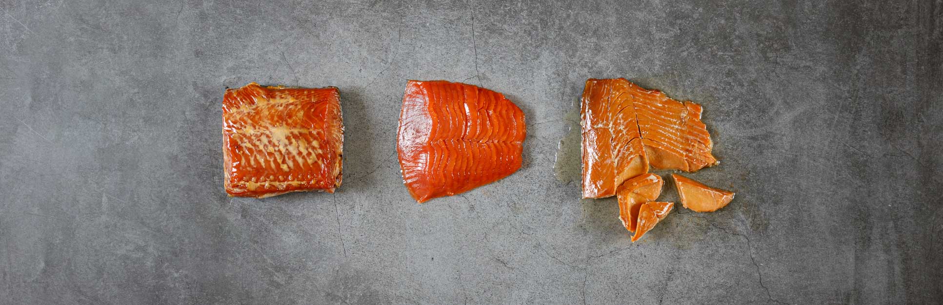 Three fillets of smoked salmon on a grey cement surface