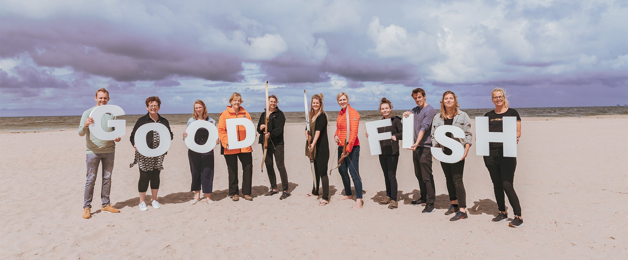 The scientists and crew from the Good Fish Foundation stand on a beach, holding letters that spell their organization's name