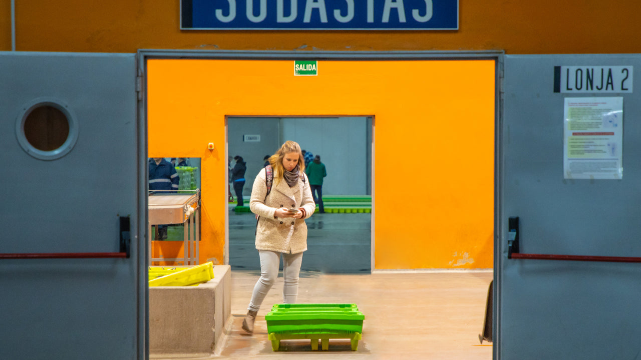 A scientist from Good Fish Foundation stands in warehouse with orange walls and examines recent fish harvest in a green plastic container
