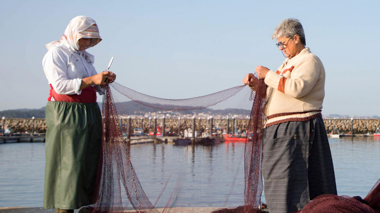 Two workers in woolen sweaters and heavy working skirts stand together repairing a fishing net