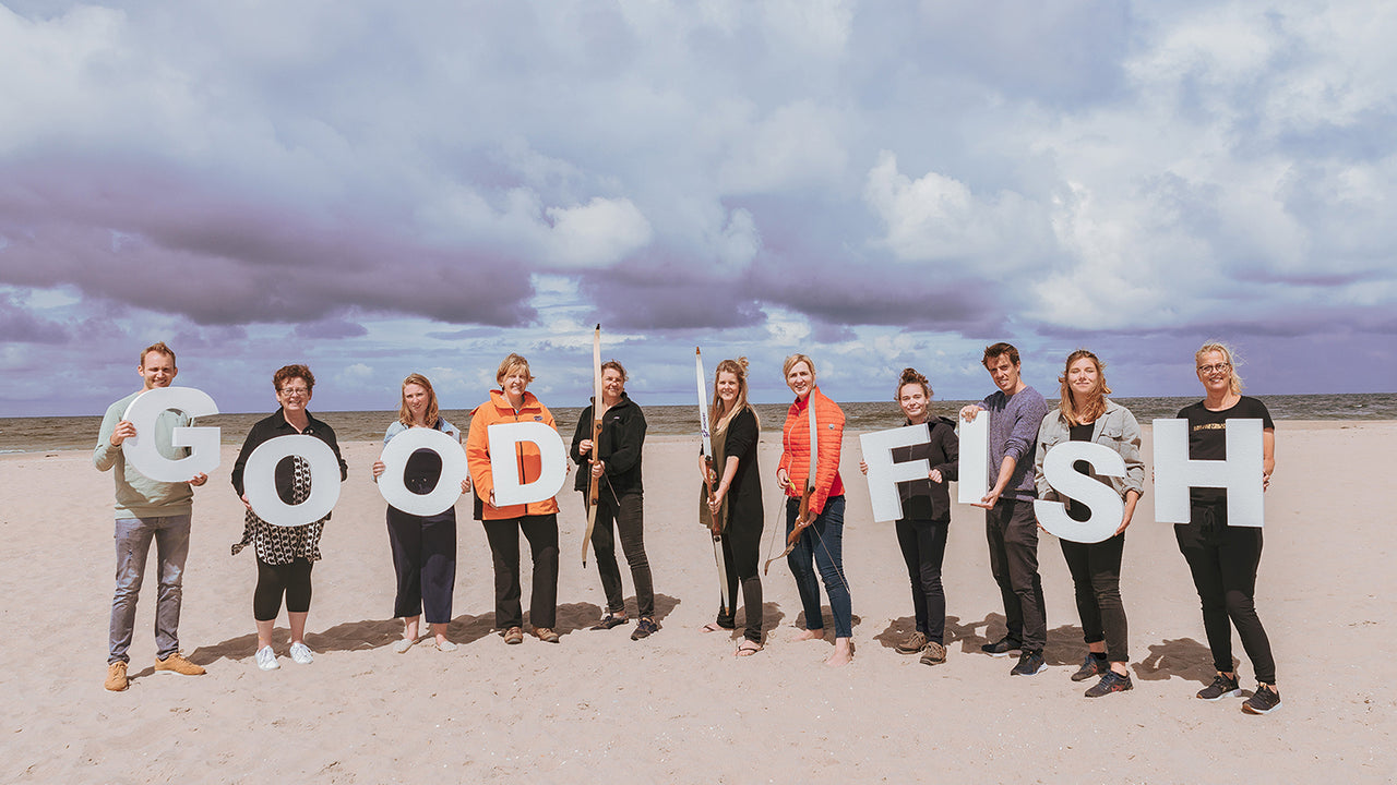 A group of people stand on a beach holding large letters that spell out Good Fish