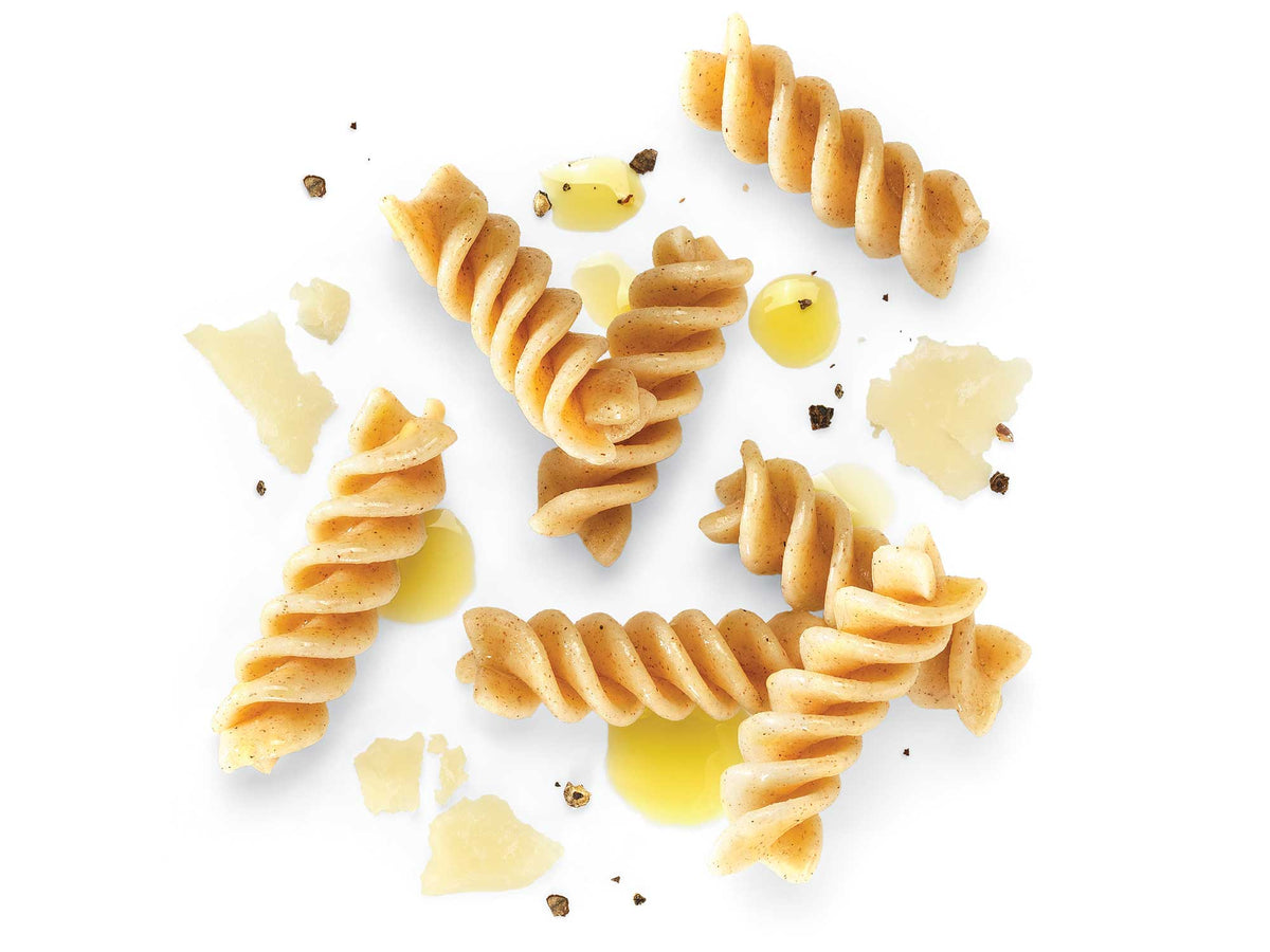 Pieces of Patagonia Provisions Organic Fusilli Pasta, with drops of olive oil, parmesan shavings, and black pepper on a white surface