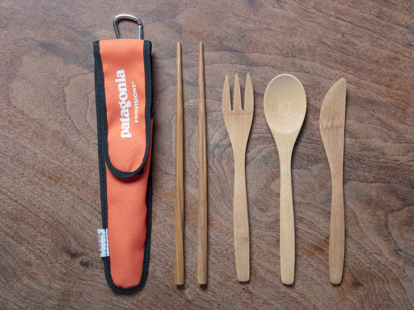All bamboo utensils with orange to-go sleeve on wood background.