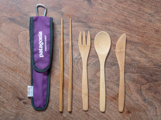 All bamboo utensils with purple to-go sleeve on wood background.