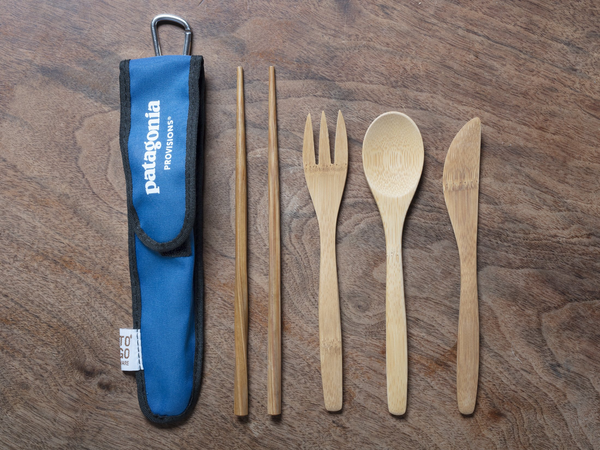 All bamboo utensils with purple to-go sleeve on wood background.