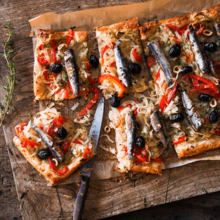 Patagonia Provisions Lemon Olive Spanish White Anchovies top a tart with olives, onions, red pepper and lemon, served on parchment paper on a wooden board